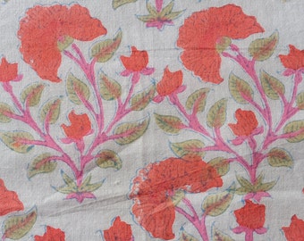 Op de afbeelding: Close-up van een stof met een herhalend bloemenpatroon. Grote koraalkleurige bloemen en kleinere knoppen zijn verbonden door roze stelen en groene bladeren. De achtergrond is lichtbeige.
