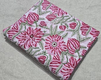 May include: Folded fabric with a floral pattern. The design features large pink flowers with dark red centers and accents, along with green leaves and buds, set against a white background. The fabric is likely cotton or linen.