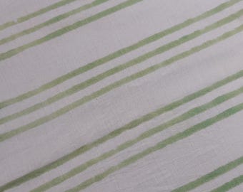 May include: Close-up of a white fabric with diagonal, unevenly spaced, light green stripes. The stripes vary in width and have a slightly textured appearance, creating a simple yet visually interesting pattern. The fabric appears to be cotton or linen.