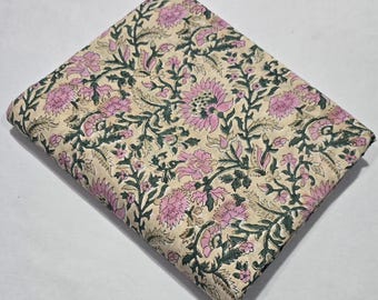May include: Folded fabric with a floral pattern. The design features pink flowers, green leaves, and stems on a beige background. The fabric is folded, showing the pattern on the top surface.
