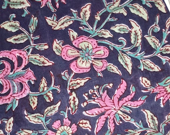 May include: Close-up of a fabric with a floral pattern. The design features pink flowers with green and blue accents on a dark blue background. The leaves and stems are in shades of green and blue.