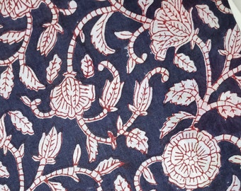 May include: Close-up of a fabric with a repeating floral pattern. The design features white flowers and leaves with red outlines and stems against a dark blue background. The fabric has a soft, textured appearance.