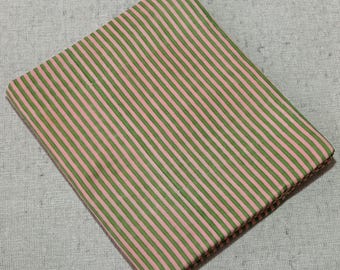May include: Folded fabric with a repeating pattern of green and pink vertical stripes. The fabric is folded neatly, and the stripes are evenly spaced. The fabric is likely cotton or a similar material, and the colors are soft and muted.