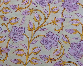 May include: Close-up of a floral pattern fabric. The design features large, stylized purple flowers with detailed petals, yellow stems, and leaves against a pale yellow background. The pattern repeats across the fabric, creating a cohesive design.
