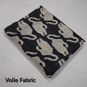 May include: Black voile fabric with a repeating pattern of off-white tiger illustrations. The fabric is folded, showing the pattern's design. The text "Voile Fabric" is printed at the bottom of the image.