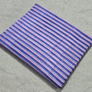 May include: Folded fabric with a striped design. The fabric displays alternating stripes of blue, pink, and white. The fabric is neatly folded, highlighting the pattern. The background is a neutral, light-coloured surface.