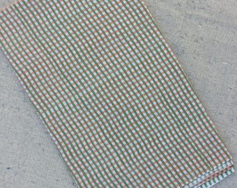 May include: Folded fabric with a green, white, and peach gingham pattern. The fabric is folded neatly, showcasing the repeating checkered design. The fabric is likely cotton or linen, suitable for home decor or apparel.