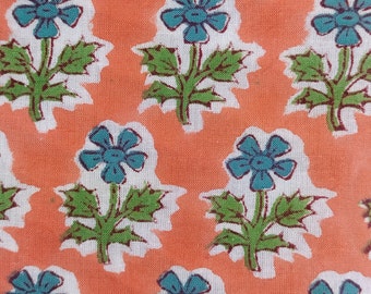 May include: Close-up of a fabric with a repeating floral pattern. Teal blue flowers with green stems and leaves are set against a peach-colored background. The flowers are outlined in white.