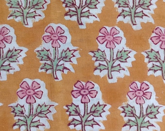 May include: Close-up of a fabric with a repeating floral pattern. The flowers are pink with green stems and leaves, set against a white background. The background is a warm, golden-orange color, creating a vibrant and eye-catching design.