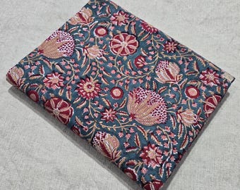 May include: Folded fabric with a teal background and a floral pattern in shades of red, pink, and tan. The design features stylized flowers and leaves, creating a detailed and colorful textile.