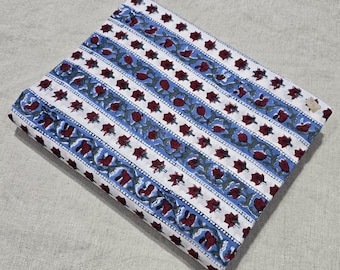 May include: Folded fabric with a white background, featuring blue stripes and floral patterns in red and green. The fabric is likely cotton or a similar material, suitable for sewing or crafting projects.
