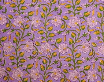 May include: A repeating floral pattern on a lavender background. White flowers with yellow centers and green stems and leaves are arranged in vertical rows. Yellow accents are visible on the leaves. The design is suitable for fabric or wallpaper.