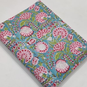 May include: Folded fabric with a floral pattern. The fabric features a teal background with pink flowers and green leaves. The flowers have a detailed design with multiple petals and are evenly spaced across the fabric.