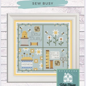 May include: Framed cross-stitch art with a light blue background, featuring bees, flowers, and sewing-related items. The text "SEW BUSY" is displayed above the artwork. The design includes the text "HONEY" and "White House Stitchery".