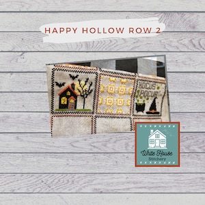 Może przedstawiać: Próbka haftu krzyżykowego z motywem Halloween. Próbka przedstawia dom, drzewo, kapelusz czarownicy i słowa "Hocus Pocus". Próbka jest oprawiona w białą ramę i ma etykietę "White House Stitchery".