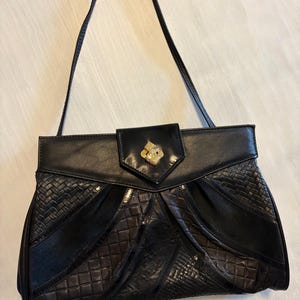 May include: Black leather handbag with a top handle. The bag features a geometric design with various textures and a gold-coloured clasp. The bag's design includes woven and quilted leather panels. The bag is a vintage style.
