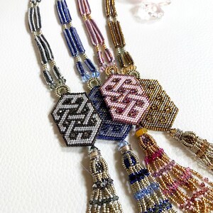 May include: Four beaded necklaces with geometric patterned pendants and tassel ends. The necklaces are in shades of gray, blue, pink, and gold.