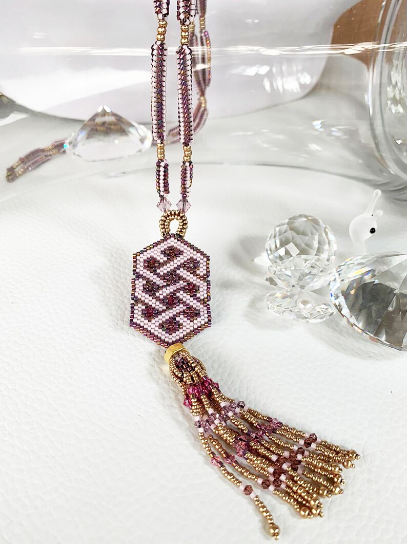 May include: A pink and gold beaded necklace with a geometric pendant and a tassel. The pendant is a hexagon shape with a repeating pattern of pink and white beads. The tassel is made of pink and gold beads.