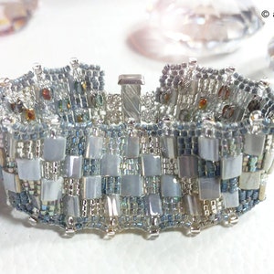 May include: A silver and blue beaded bracelet with a clasp closure. The bracelet is made with small, square beads in a checkered pattern.