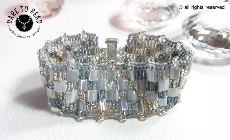 May include: A silver and blue beaded bracelet with a clasp closure. The bracelet is made with small, square beads in a checkered pattern.