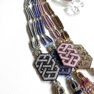 May include: A multi-strand beaded necklace with a geometric pattern and tassels. The necklace is made of silver, blue, purple, and gold beads. The tassels are made of silver, blue, and purple beads.