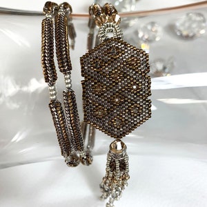 May include: A pair of beaded bracelets with a silver and gold color scheme. The bracelets are made of small, round beads and have a geometric pattern. The bracelets are accented with a tassel.