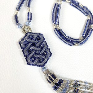 May include: A blue and silver beaded necklace with a tassel and a geometric pendant. The pendant is made of blue and silver beads and has a woven design.