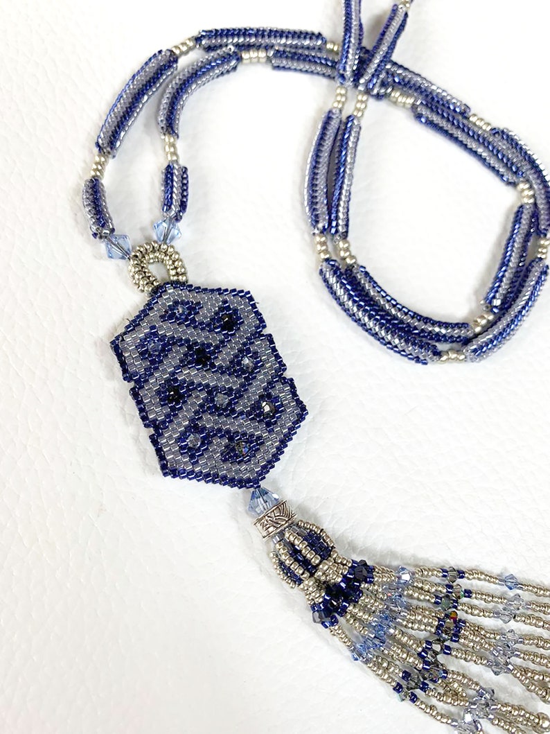 May include: A blue and silver beaded necklace with a tassel and a geometric pendant. The pendant is made of blue and silver beads and has a woven design.