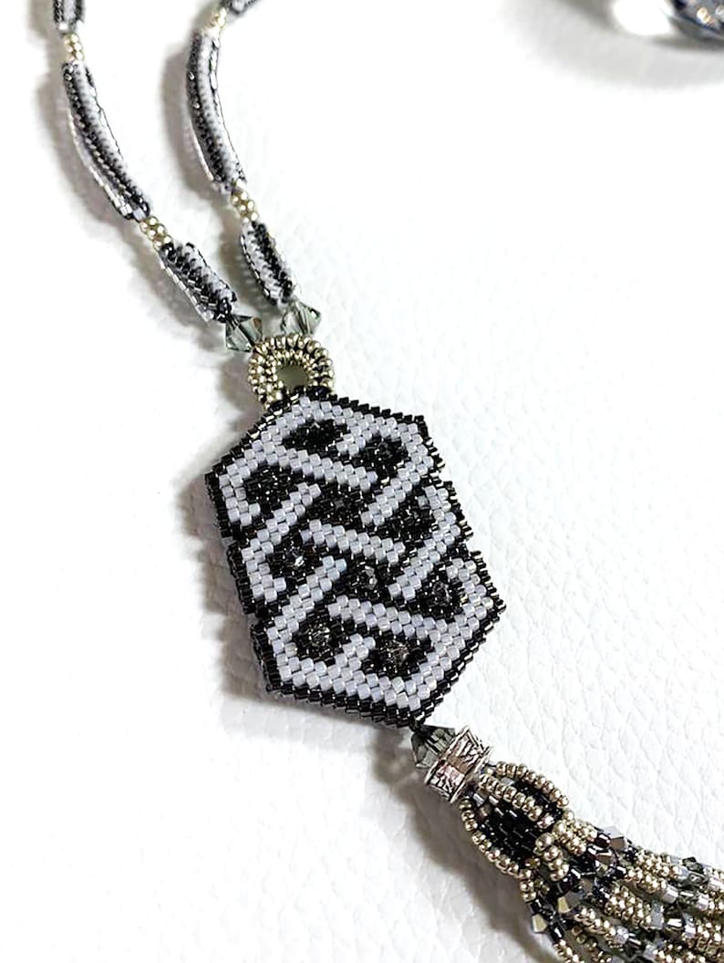 May include: A black and white beaded necklace with a geometric pendant and a tassel. The pendant is made of small black and white beads and has a geometric pattern. The tassel is made of black, white, and silver beads.