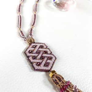 May include: A pink and gold beaded necklace with a geometric pendant and a tassel. The pendant is a hexagonal shape with a pink and gold pattern. The tassel is made of pink and gold beads.