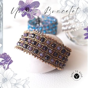Może przedstawiać: Prezentowany jest bransoletka z koralików z napisem "Ursula Bracelet". Bransoletka ma złotą podstawę z rzędami fioletowych i czarnych koralików. Spoczywa na białej powierzchni, z kwiatowymi akcentami w tle. Widoczne jest logo marki "Dare to Bead".