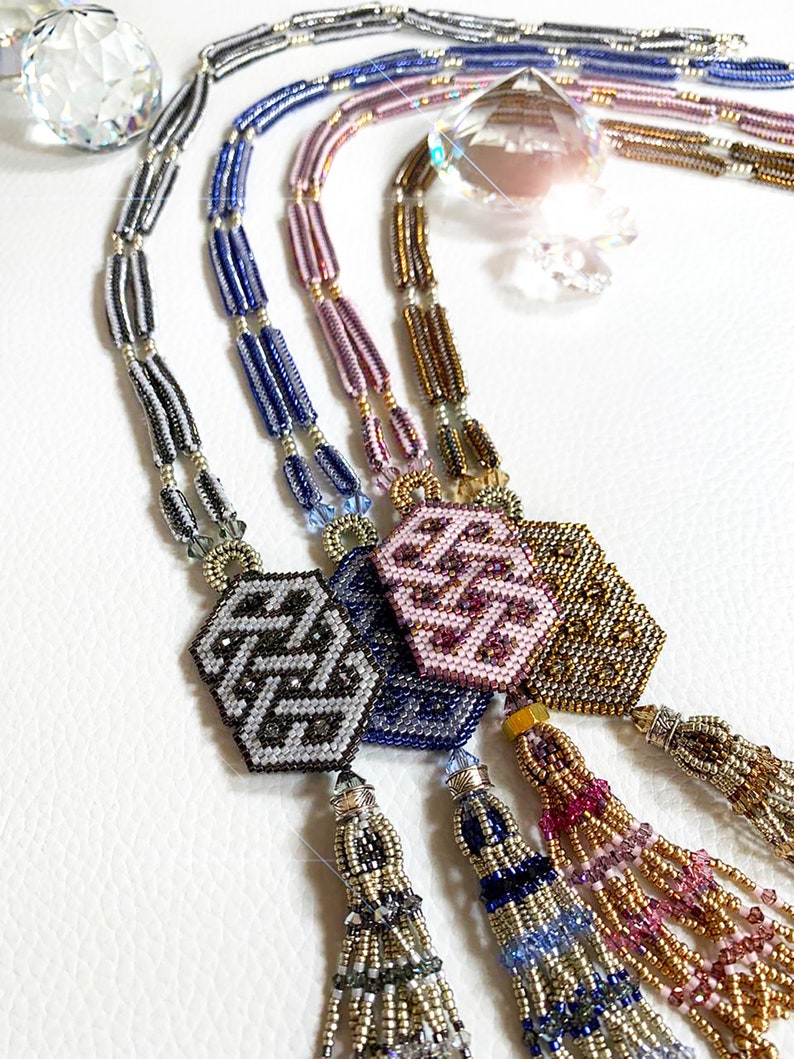 May include: Four beaded necklaces with geometric patterned pendants and tassel ends. The necklaces are in shades of gray, blue, pink, and gold.
