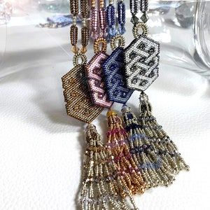 May include: Five beaded necklaces with hexagonal pendants and tassel ends. The pendants are in shades of gold, pink, blue, and gray. The tassels are in shades of gold, pink, blue, and silver.