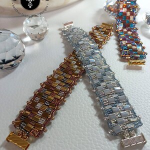 May include: Three reversible beaded bracelets with a checkered pattern. The bracelets are in shades of silver, gold, and brown. The bracelets are on a white surface with the text "REVERSIBLE" below them.