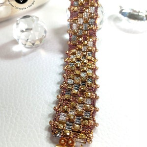 May include: A gold, silver, and pink beaded bracelet with a toggle clasp. The bracelet is made with small, faceted beads and has a checkered pattern.