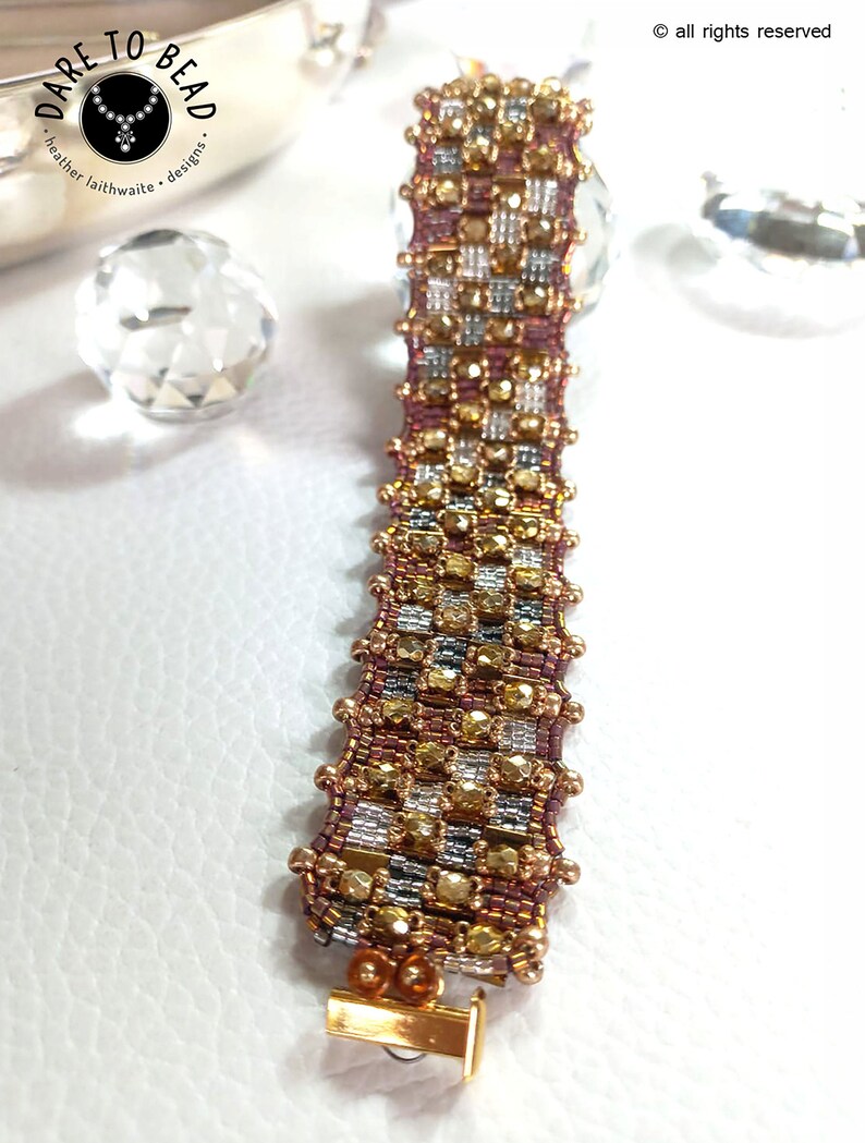 May include: A gold, silver, and pink beaded bracelet with a toggle clasp. The bracelet is made with small, faceted beads and has a checkered pattern.