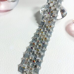 May include: A silver and blue beaded bracelet with a silver clasp. The bracelet is made with small, iridescent beads and has a geometric pattern.