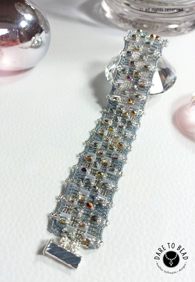 May include: A silver and blue beaded bracelet with a silver clasp. The bracelet is made with small, iridescent beads and has a geometric pattern.
