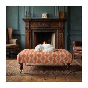 May include: A rectangular ottoman upholstered in orange fabric with a white repeating wave pattern. The piece features four dark brown turned wooden legs with brass casters. A fluffy white cat is resting on the top surface of the ottoman.