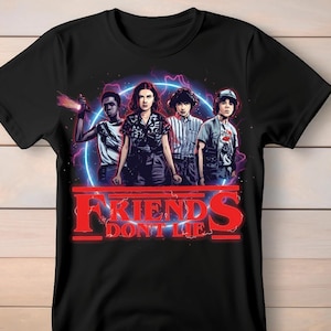 Puede incluir: Camiseta negra con un gráfico de cuatro personajes sobre un fondo azul y morado neón. El texto rojo dice "FRIENDS DON'T LIE". La camiseta está hecha de un material suave.