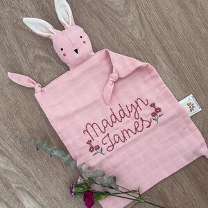 Pu&ograve; includere: Coperta di sicurezza rosa a forma di coniglio con il nome "Maddyn James" ricamato in rosso con piccoli fiori rossi.