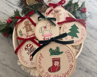 May include: A collection of round wooden embroidery hoops featuring personalized Christmas designs. Each hoop contains fabric with embroidered motifs like a gingerbread man, rocking horse, tree, candy cane, and stocking, accented with red or green bows.