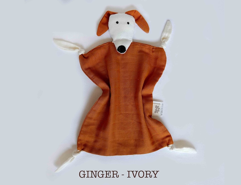 May include: A soft, brown and ivory plush dog toy with a white face and black nose. The toy has four white ties attached to the corners.