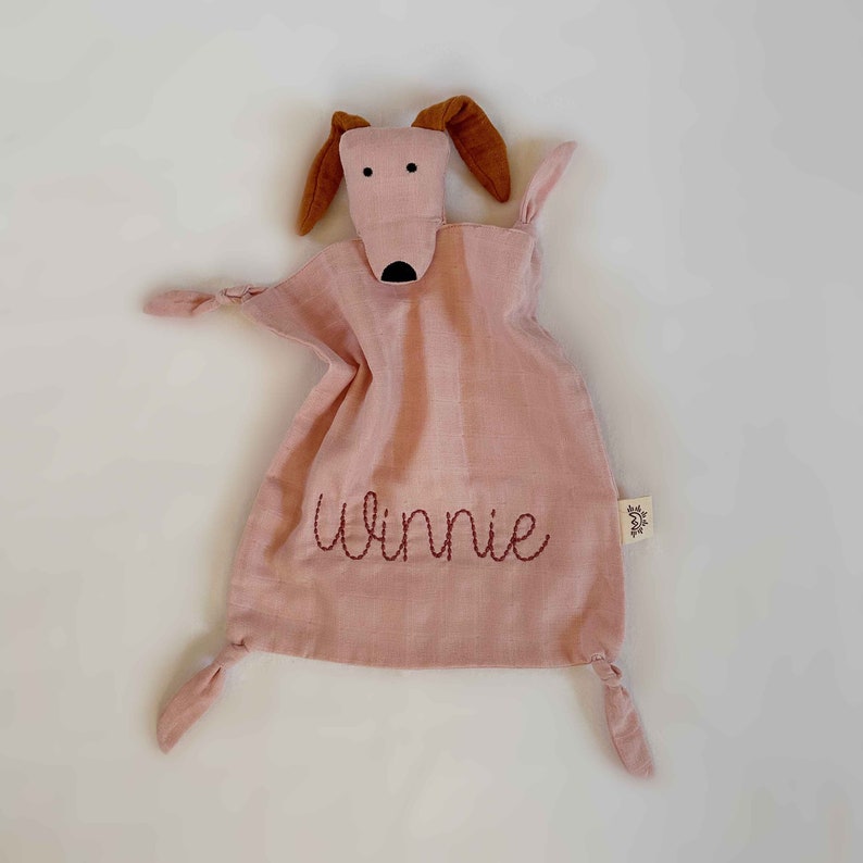 May include: A pink muslin baby security blanket with a brown felt dog face and ears. The blanket has knotted corners and the name "Winnie" embroidered in red thread.