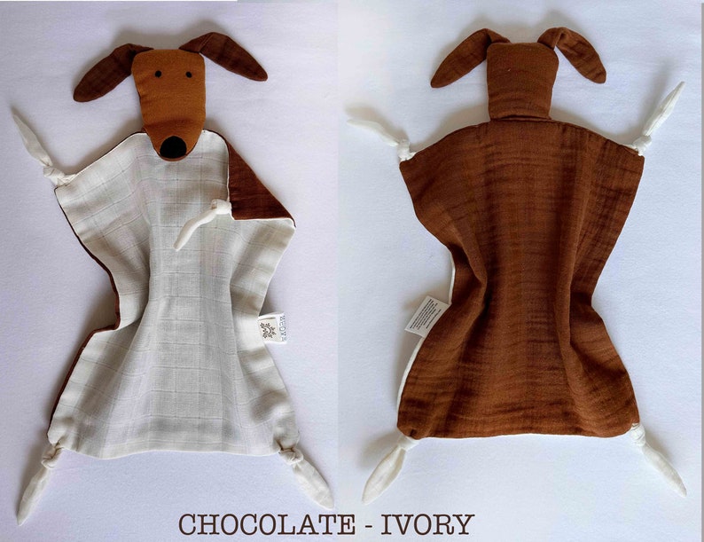 May include: A brown and white muslin baby security blanket with a brown dog head attached. The blanket has a white muslin center and brown muslin edges. The dog head has a brown nose and black eyes. The blanket has a tag that says "VEDUTA".