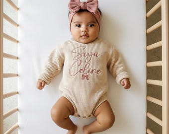 May include: A beige long-sleeved ribbed knit bodysuit featuring the embroidered text Siya Celine in a dusty rose script font with a small matching bow icon below the name, paired with a coordinating dusty rose fabric bow headband.