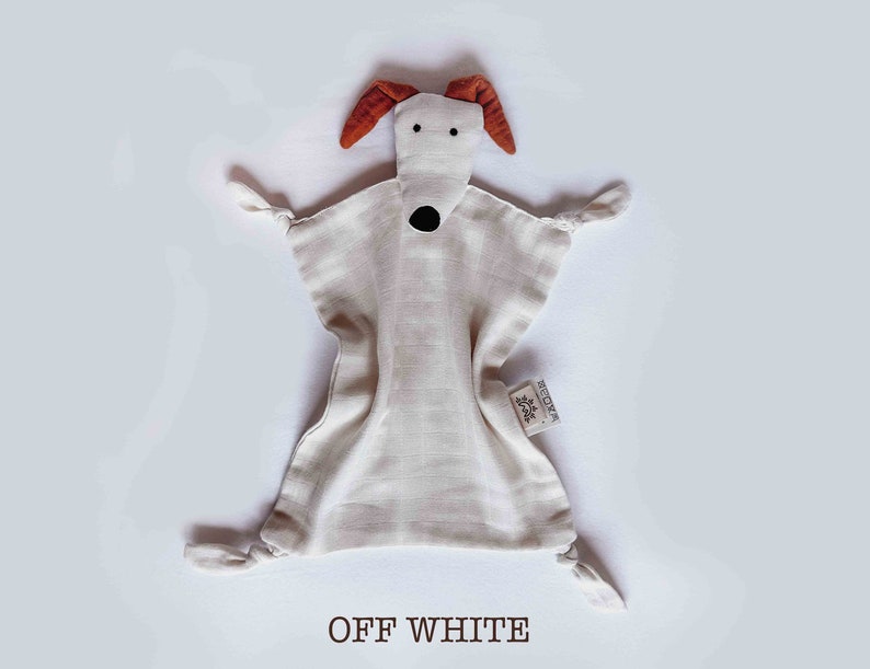 May include: Off-white muslin baby security blanket with a dog face and brown ears. The blanket has knotted corners and a small tag that says "REDOMA".