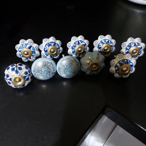 May include: Assortment of ten ceramic drawer knobs with blue and white floral patterns and gold accents. The knobs are arranged in two rows on a black surface.