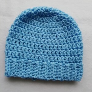 May include: A light blue crocheted beanie hat. The hat is made of a soft, textured yarn and features a ribbed brim. The hat is a solid color and appears to be handmade.