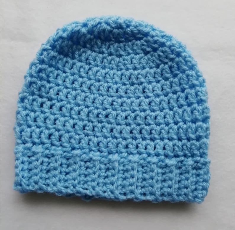 May include: A light blue crocheted beanie hat. The hat is made of a soft, textured yarn and features a ribbed brim. The hat is a solid color and appears to be handmade.